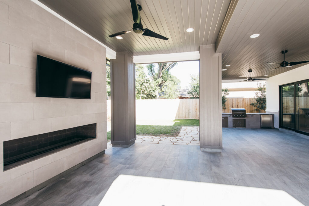 Covered patio featuring a large linear outdoor fireplace with a stone surround and honed tile floors locate in Briarcroft Subdivision in Houston.