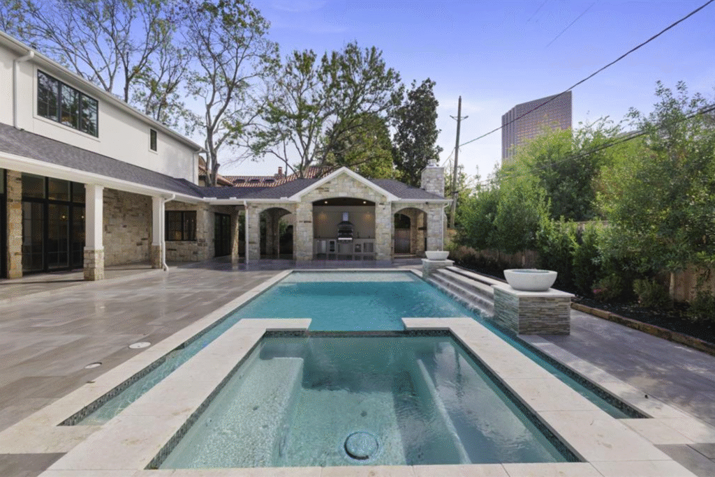 Luxury backyard pool with a raised spa, water spillways, and fire bowls next to a limestone patio cover, showcasing premium outdoor living spaces in Houston's Tanglewood neighborhood.