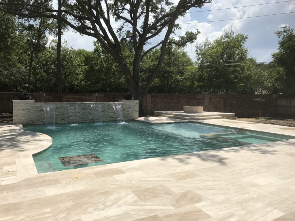 Luxury travertine pool deck and elevated fire pit in a classic brick pattern for a Tanglewood subdivision home in Houston, TX.