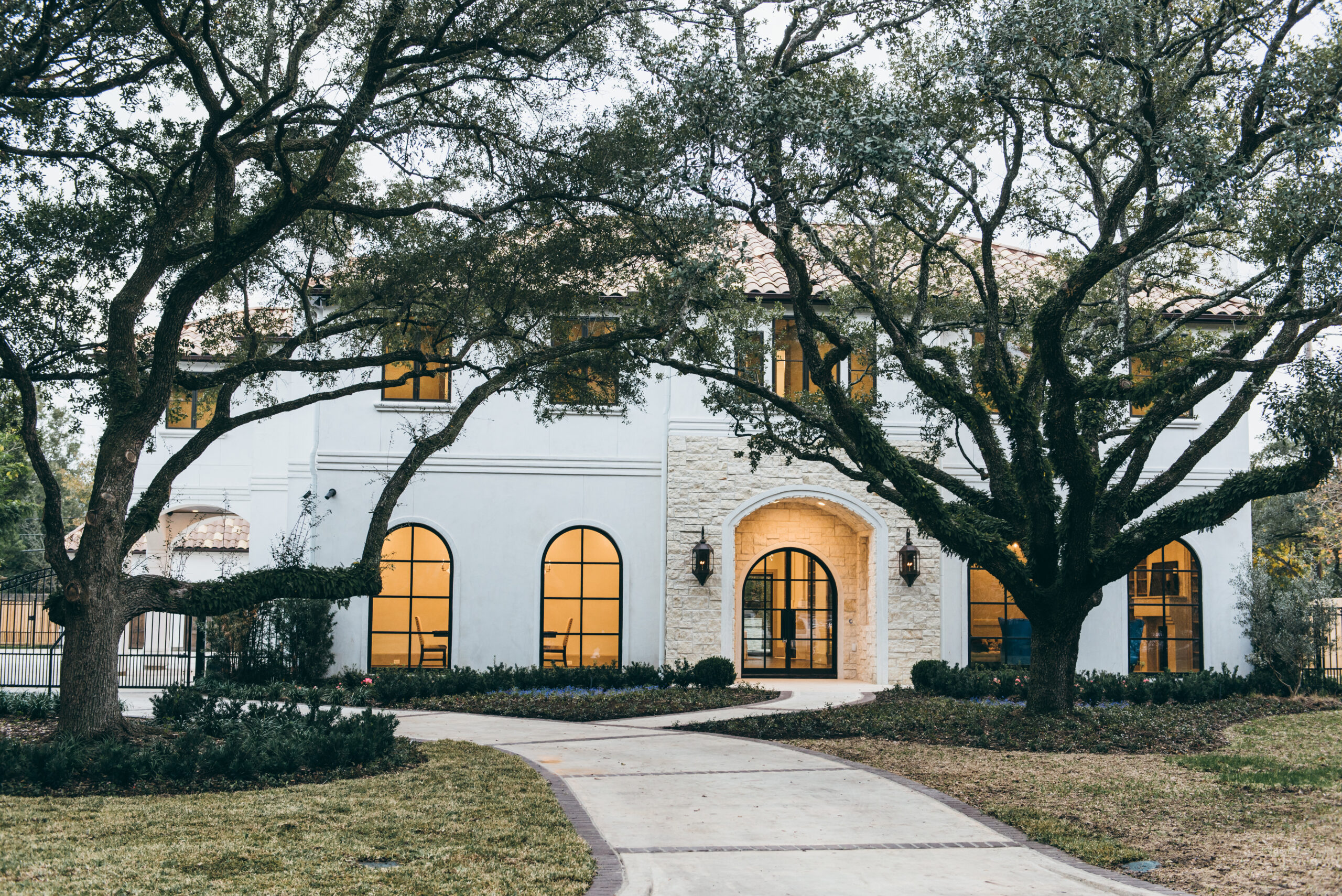 A large luxury stucco home in the Tanglewood subdivision featuring a sweeping circular driveway with detailed brick accents and borders, showcasing high-end custom paver and concrete walkway designs.