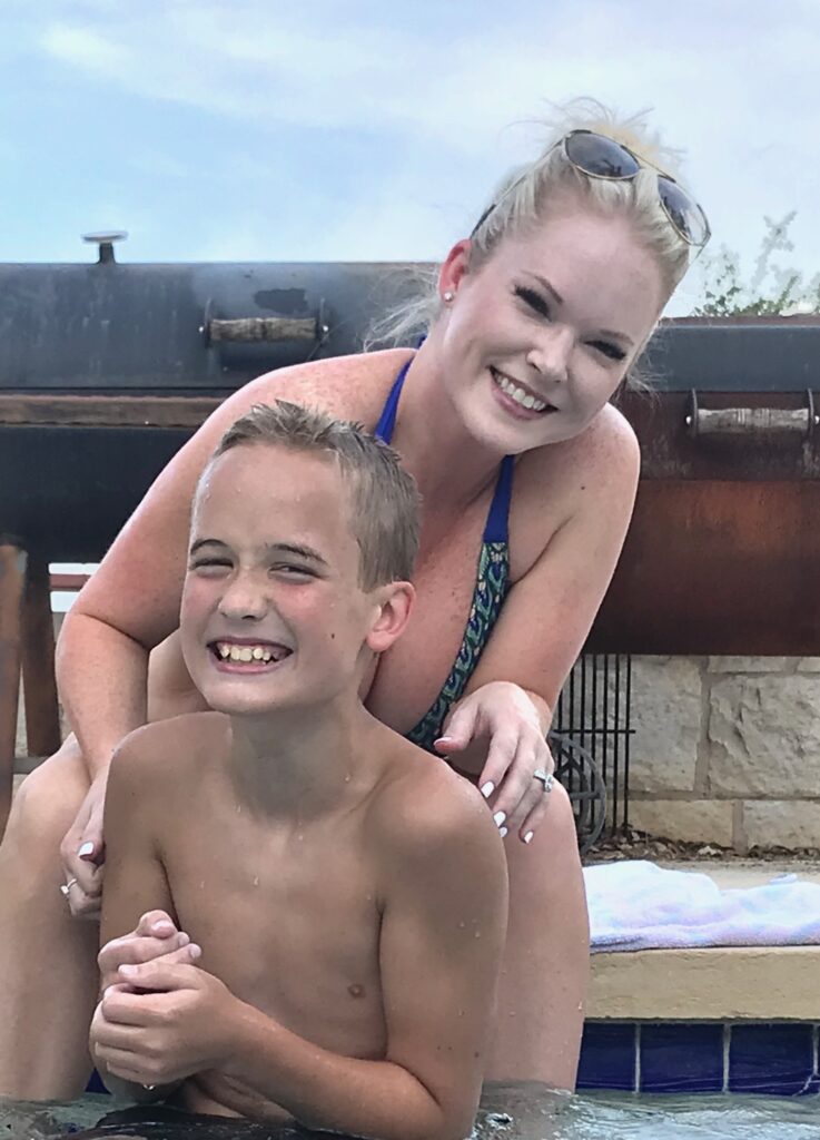 Family-Friendly Custom Pool Design: Happy Mother and Son Relaxing on Pool Steps and travertine coping A smiling young boy sits on the shallow tanning ledge pool steps with his happy mom sitting behind him on the travertine pool coping during a sunny day in Houston Texas area.