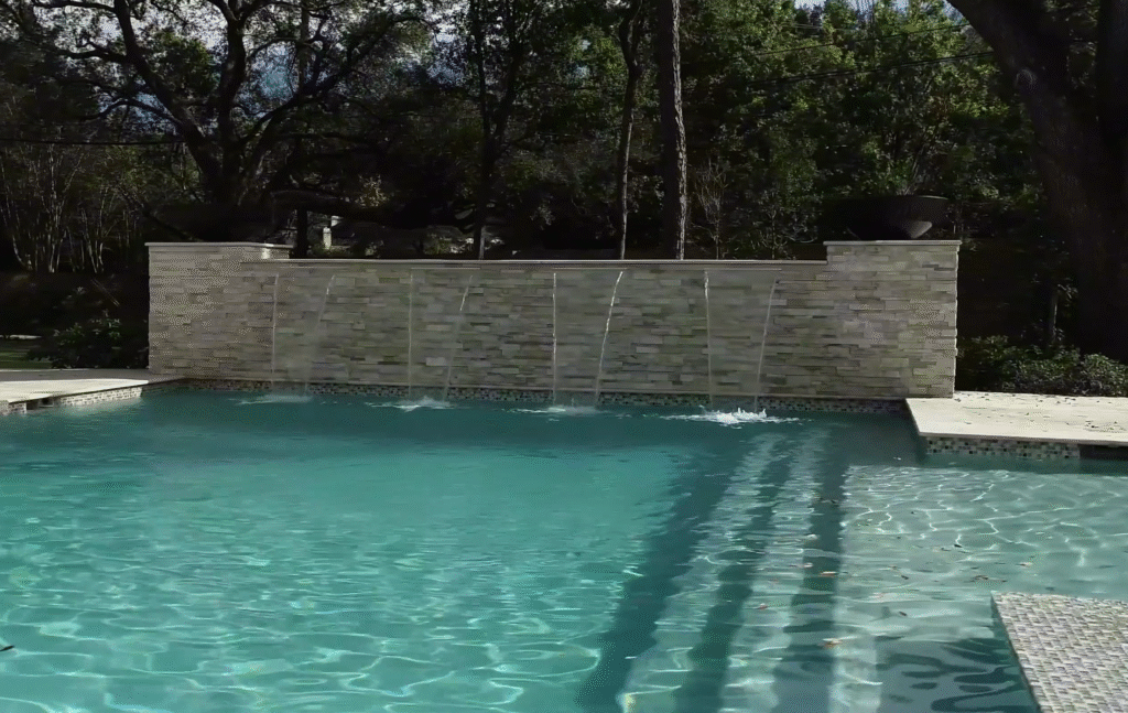 custom-luxury-pool-5ft-raised-beam-sheer-descents-fire-bowls Custom luxury swimming pool featuring a five-foot split-faced stone raised beam wall, four three-foot sheer descent waterfalls, and two flaming fire bowls in a modern Houston backyard oasis.