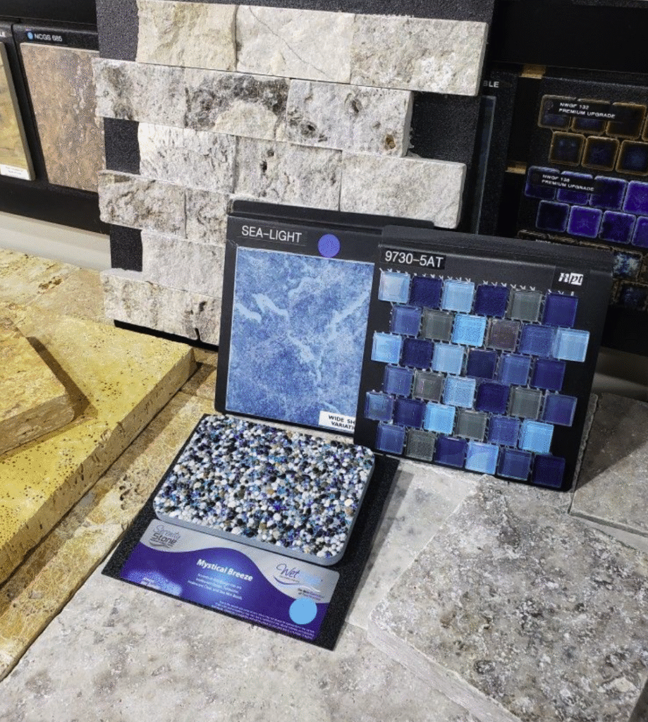 LuxScape Custom Luxury Pool Material Selection with Wet Edge Finish Curated swimming pool material selections featuring travertine pool coping, split face ledger stone for a raised beam wall, blue/grey glass mosaic spa surround, blue waterline tile, and Wet Edge premium pebble finish from the Serenity Stone collection.