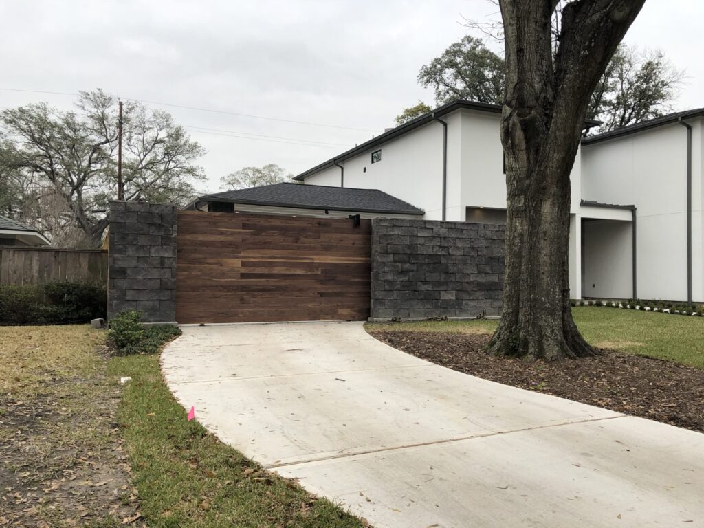Custom Walnut Access Gate and Stone Privacy Wall in Briarcroft A custom walnut wood access gate with horizontal slats set into a natural stone privacy wall in the Briarcroft neighborhood of Houston, TX.