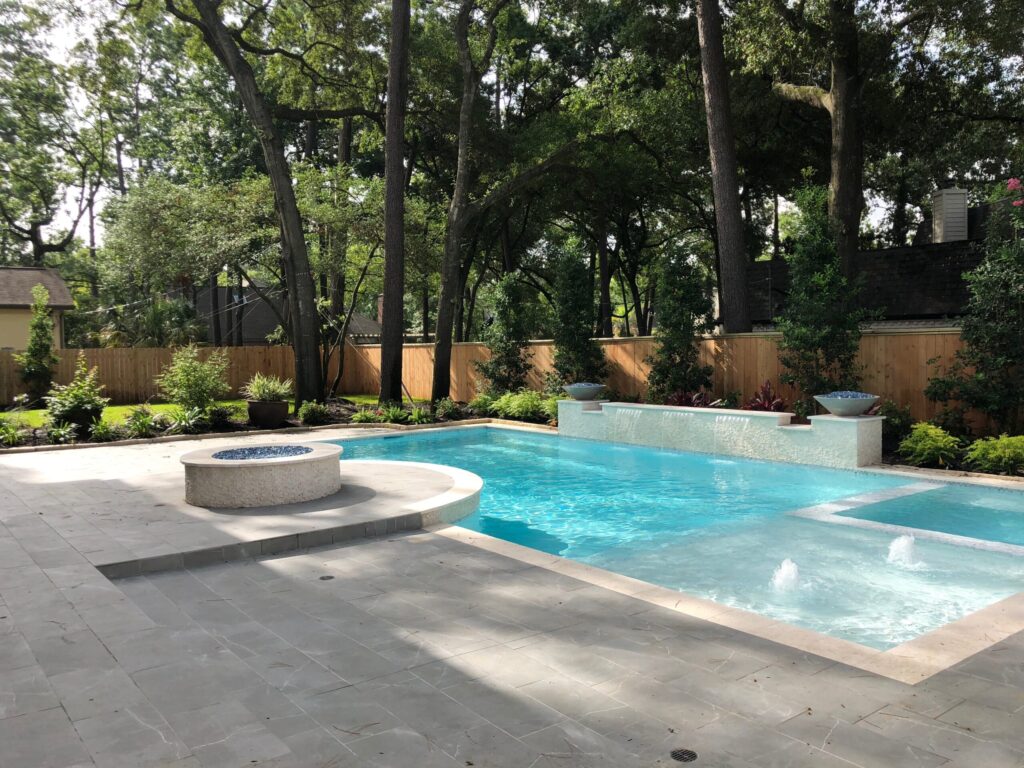 Medium grey concrete pavers in a brick pattern around a custom pool and elevated fire pit for a Katy, TX backyard