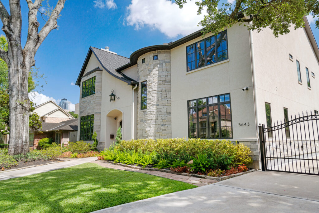 A composition shingle roof with curved eave details on a two-story stone and stucco home, Luxscape Outdoor Builders serving Houston, TX.