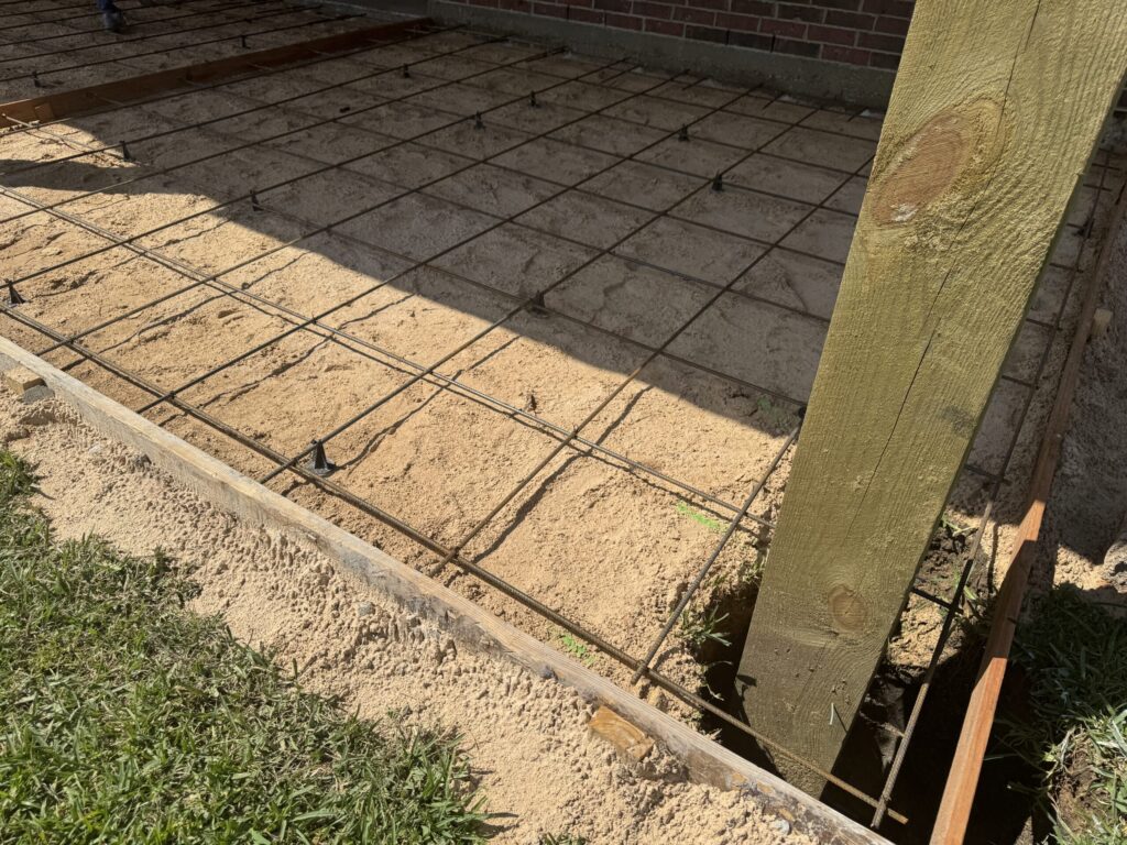 Custom concrete patio ready for the pour, with wood forms set, gravel base compacted and a tied steel rebar grid in place, designed for Cypress homeowners by Luxscape Outdoor Builders serving Houston, TX.