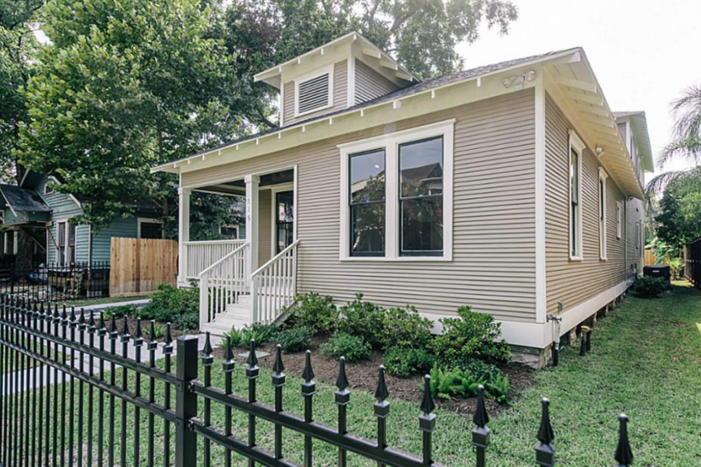 A remodeled Historic Heights bungalow with a covered front porch, new siding and a black iron fence, Luxscape Outdoor Builders serving Houston, TX.